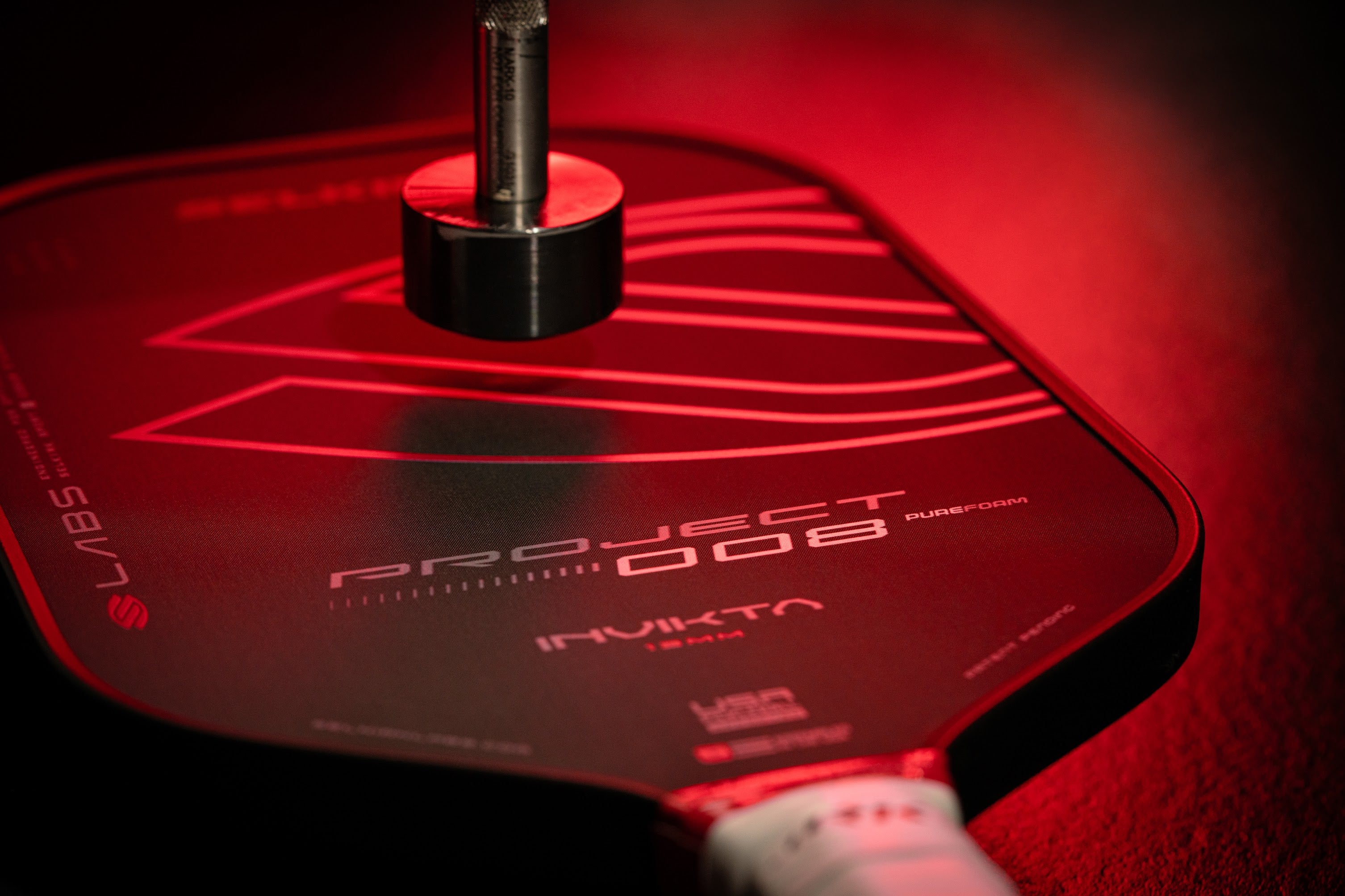 Close-up of a pickleball paddle with a sleek design and red accents, highlighting the Project 008 and Invikta branding.